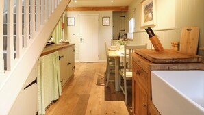 A kitchen with wooden floors, a dining table, chairs, a white refrigerator, and a staircase with white railings. - The Hayloft - Beautiful Barn Stay (Ashford)