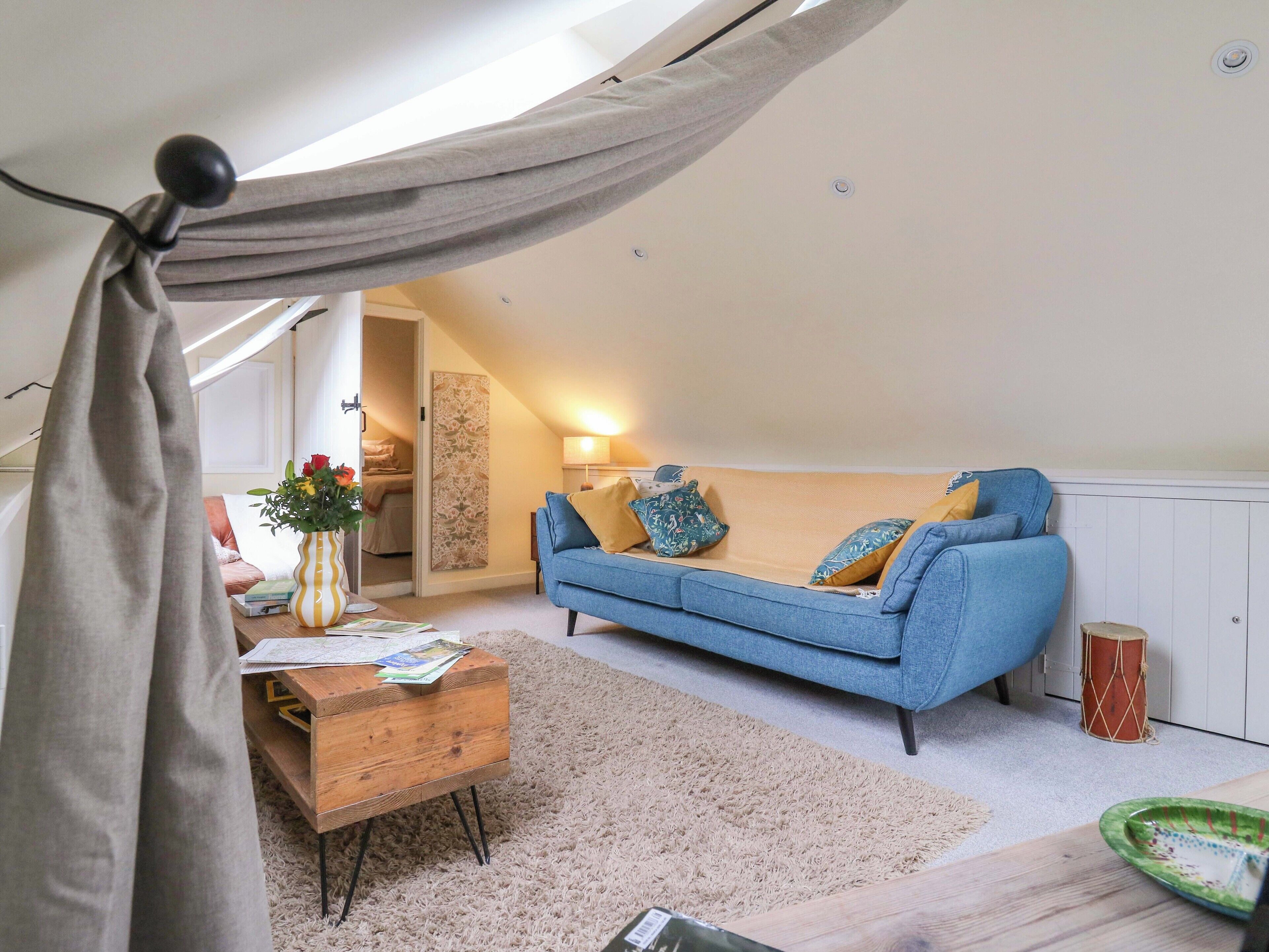 A cozy loft bedroom with a blue sofa, a wooden chest of drawers, and a hanging hammock.