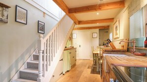 A staircase with wooden railings leading to a second floor, a kitchen area with wooden countertops and a sink, and a dining area with a table and chairs. - The Hayloft - Beautiful Barn Stay (Ashford)