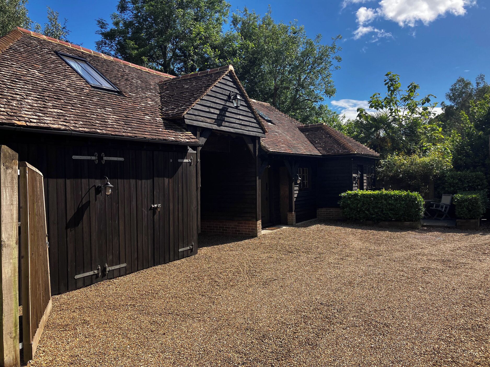 A rustic building with a gravel driveway, wooden doors, and a sloped roof.