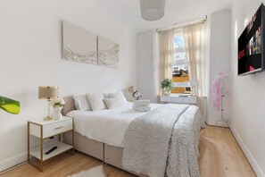 Una camera da letto moderna con un letto, un comodino e una TV fissata al muro.