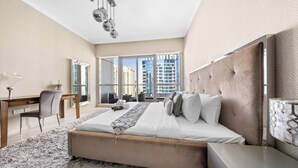 A modern bedroom with a large bed, a desk, and a view of tall buildings. - StayShort - 2BR in Dubai Marina that Sleeps 6 with Water Views! (Dubai Marina)