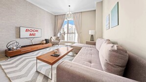 A modern living room with a sofa, a coffee table, a TV, and a view of buildings outside. - StayShort - 2BR in Dubai Marina that Sleeps 6 with Water Views! (Dubai Marina)