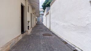 A narrow alleyway with a paved path, flanked by buildings with white walls and a potted plant. - Apartamento Pet Friendly com Garagem no Nova Su a (Belo Horizonte)