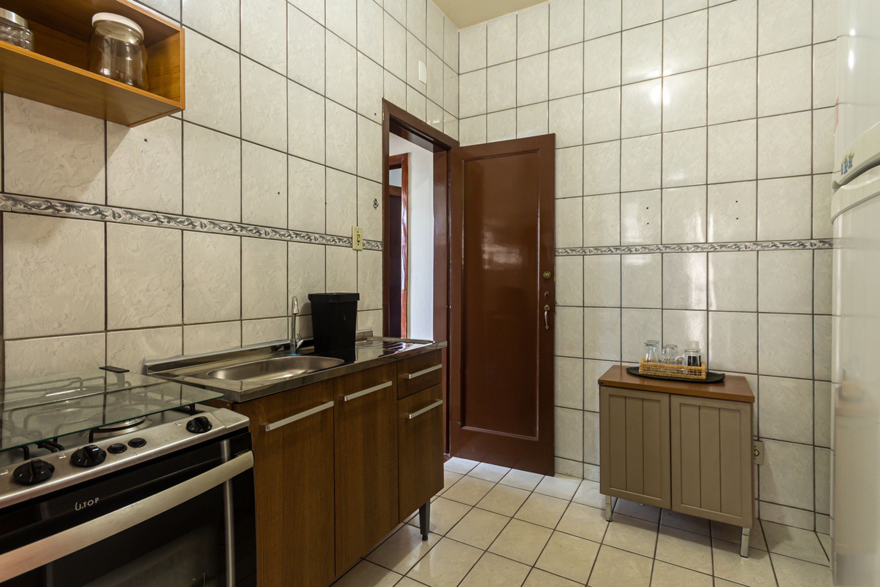 A kitchen with a gas stove, a sink, wooden cabinets, and a small refrigerator.