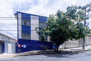 A building with a blue and white facade, a metal fence, and a tree in front. - Apartamento Pet Friendly com Garagem no Nova Su a (Belo Horizonte)