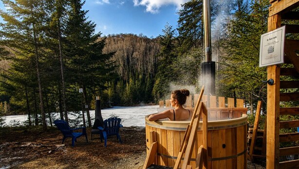 Ein Whirlpool inmitten von Bäumen, mit einer Holzterrasse und Stühlen.