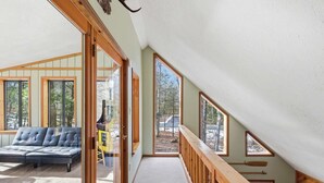 A modern interior with a loft bedroom, large windows, and a view of the outdoors. - Deer Hollow Retreat | Fireplace, Bunk Bed, Game Rm (Albrightsville)