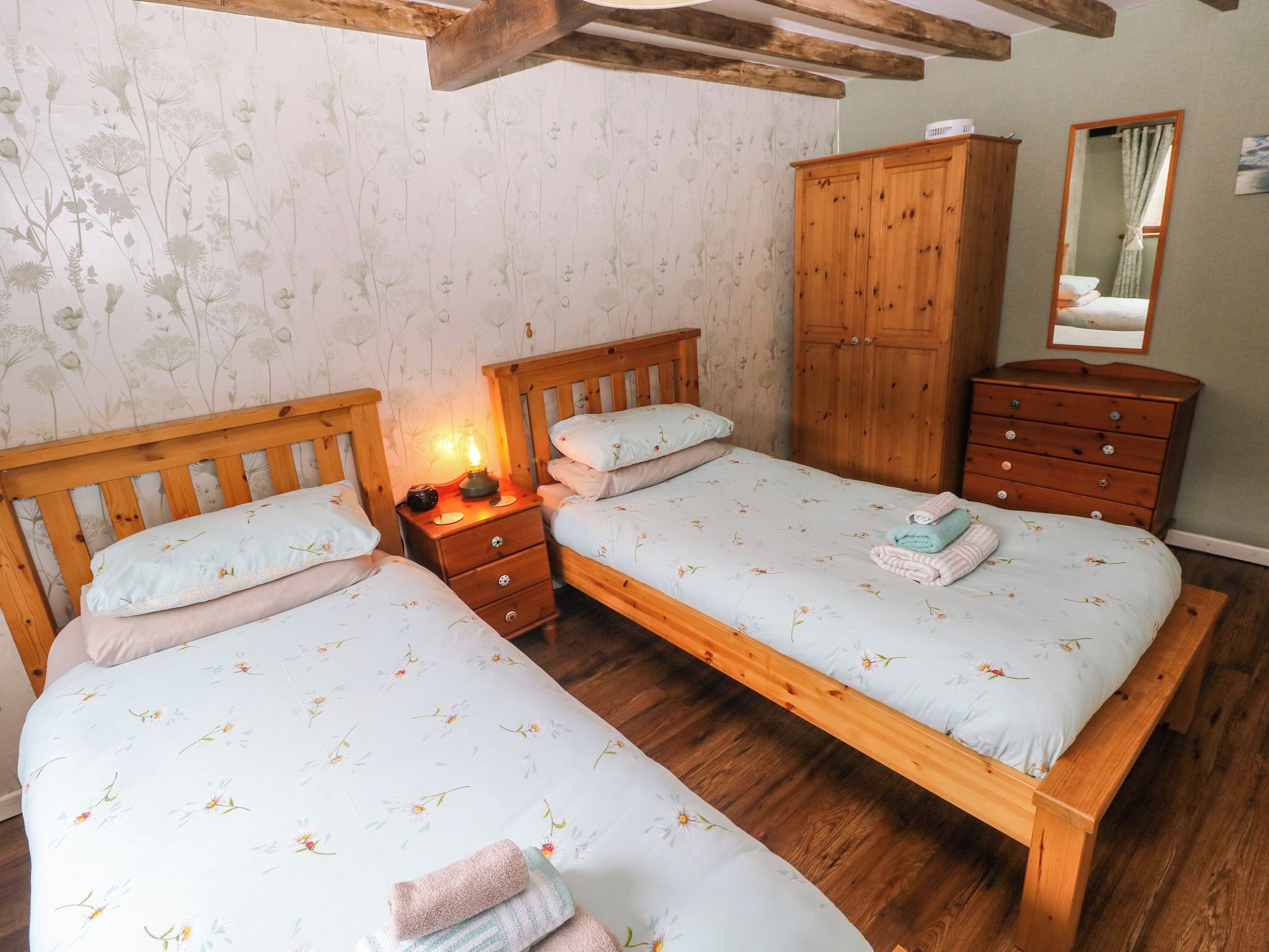 A bedroom with two wooden beds, a nightstand with a lamp, a wooden wardrobe, and a dresser.