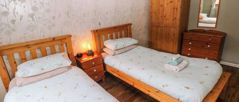 A bedroom with two wooden beds, a nightstand with a lamp, a wooden wardrobe, and a dresser.