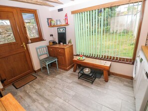 Una habitación compacta con una puerta de madera, una silla azul, un escritorio de madera pequeño, un banco y una ventana con persianas verticales.