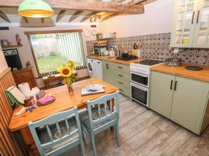 A kitchen with a wooden table, two chairs, a sink, a stove, and a window with blinds. - 2 Strand Cottages (Carmarthen)