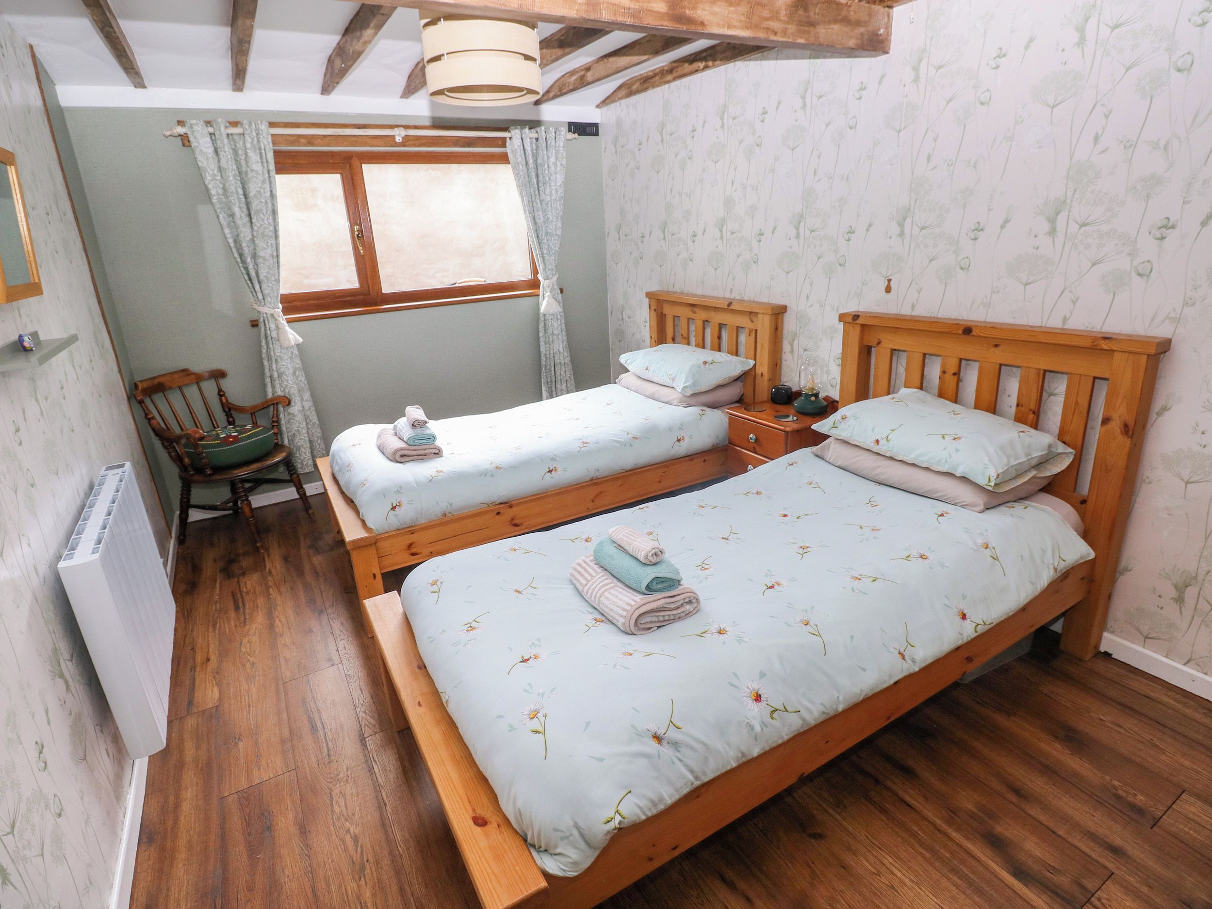 A room with two wooden beds, a chair, a window with curtains, and a radiator.