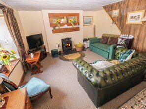A living room with a green sofa, a television, a fireplace, and a wooden wall.