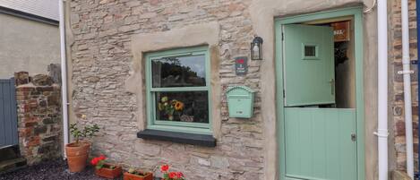 Edificio de piedra con una puerta verde, una ventana adornada con flores y un letrero que indica '2 Strand Cottage'.