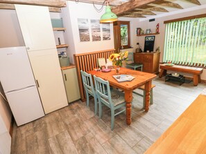 A compact kitchen with a dining table, chairs, a refrigerator, and a wooden bench.