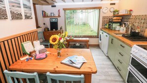 A kitchen with wooden cabinets, a dining table with chairs, a vase with flowers, and a window with a view of the outdoors.