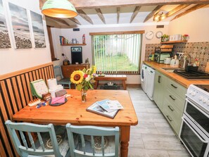 A kitchen with wooden cabinets, a dining table with chairs, a vase with flowers, and a window with a view of the outdoors.