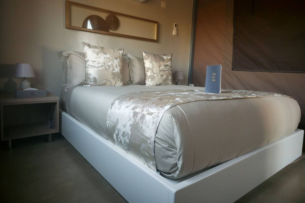 A bedroom with a large bed, a nightstand, a lamp, and a wall-mounted air conditioner.