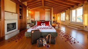 Een ruime kamer met een groot bed, een open haard en uitzicht op de omgeving.