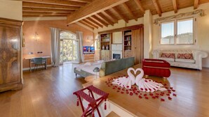 Een ruime kamer met houten vloeren, een bed, een rode bank, een eettafel met zwanenornamenten en een televisie op de achtergrond.