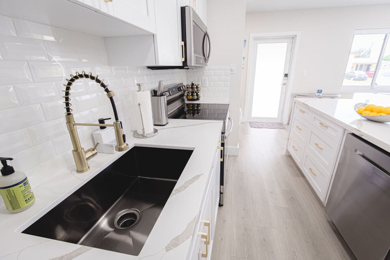 A modern kitchen with a black sink, stainless steel appliances, white cabinetry, and a window providing natural light.
