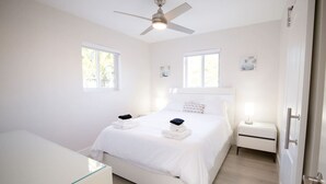 A bedroom with a bed, bedside tables, a ceiling fan, and windows.
