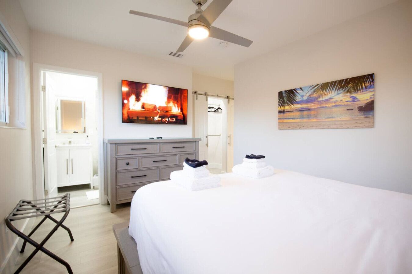 Een hotelkamer met een bed, een plafondventilator, een schilderij, een televisie en een badkamer zichtbaar door een open deur.
