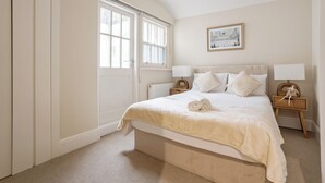 A bedroom with a large bed, two bedside tables with lamps, a window, and a painting on the wall.