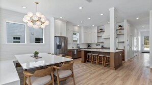 A modern kitchen with white cabinetry, a central island with stools, and a hanging light fixture. - The Gathering Place | Private Pool/Spa | Game Room | Rooftop Terrace (Santa Rosa Beach)