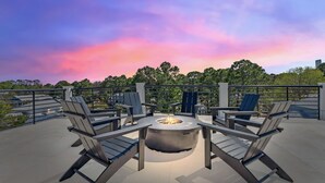 A rooftop patio with a fire pit surrounded by modern chairs, overlooking a cityscape with trees and buildings. - The Gathering Place | Private Pool/Spa | Game Room | Rooftop Terrace (Santa Rosa Beach)