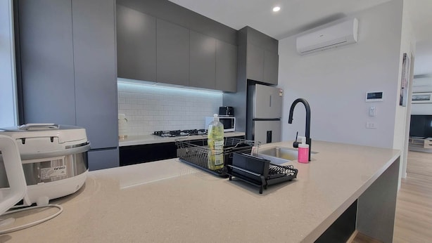 Una cocina moderna con gabinetes grises, un lavamanos de acero inoxidable, un microondas y una estufa a gas.