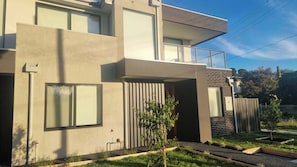 A modern two-story building with large windows, a flat roof, and a small garden area with young trees. - Brand new townhouse in Braybrook (Braybrook)