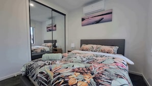 Un dormitorio con una cama grande, una mesita de noche, un espejo y un equipo de aire acondicionado en la pared.