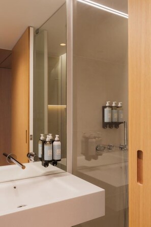 A modern bathroom with a white sink, a glass shower enclosure, and a wooden door. - Historic Lisbon at Your Door—Unwind in Pool Tranquility & Watch Light Show (Lisboa)