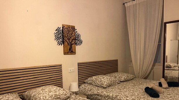 A hotel room with two beds, a tree artwork on the wall, a bedside lamp, and a mirror with a curtain.
