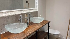 A bathroom with two glass sinks, a wooden vanity, a white toilet, and a mirror with decorative trim.