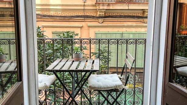 A balcony with a wooden table and two chairs, a potted plant, and a small lamp. - Designer apartment in Barcelona: Fully equipped 2-bedroom, the heart of the city (Barcelona)