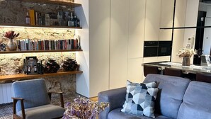A modern living room with a grey sofa, two armchairs, a coffee table, and a bookshelf against a stone wall. - Designer apartment in Barcelona: Fully equipped 2-bedroom, the heart of the city (Barcelona)