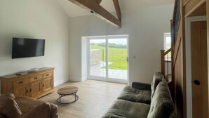 Un salón con televisor de pantalla plana, mueble de madera, sofá de cuero, mesa de centro redonda y puerta corredera de vidrio que da a un patio.