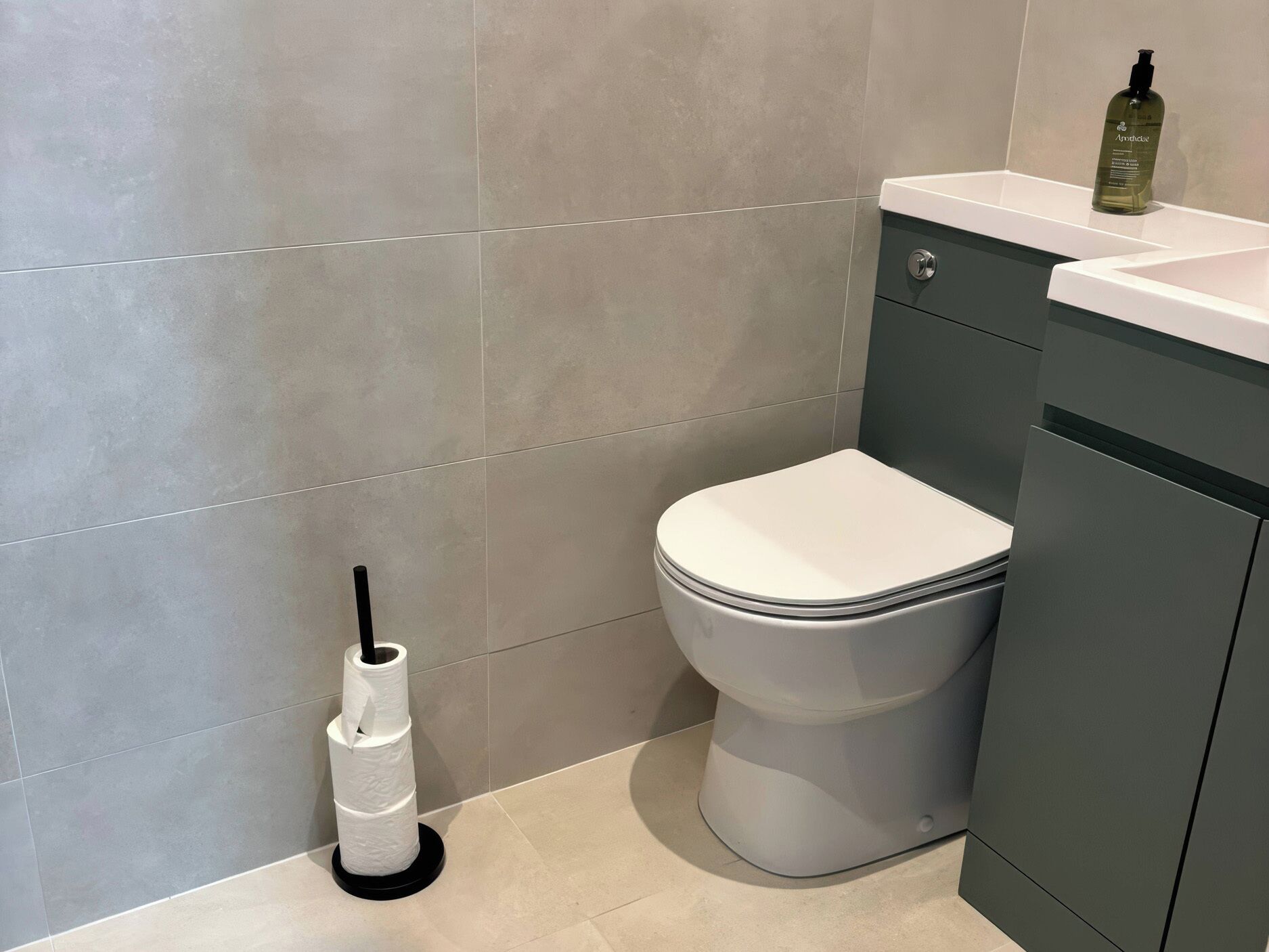Ein modernes Badezimmer mit Toilette, Papierhalter und einer Handseife am Waschbecken.