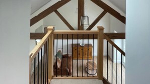 Dormitorio tipo loft con vigas de madera a la vista, una escalera de madera, una lámpara colgante y vistas de un dormitorio con cama y cómoda.