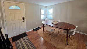 Un coin repas avec une table en bois, des chaises blanches et un tapis.