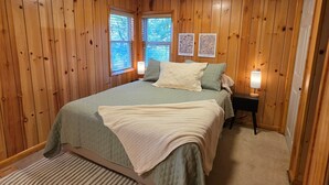 Une chambre à coucher aux murs lambrissés, avec un lit, deux lampes de chevet et deux tableaux encadrés accrochés au mur.