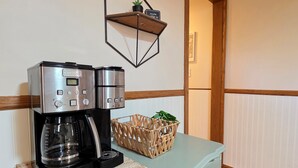 Une machine à café posée sur un comptoir, avec un panier tressé et une étagère fixée au mur au-dessus.