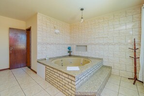 A bathroom with a large bathtub, tiled walls, a wooden door, and a towel on the tub. - Casa com Piscina e Churrasqueira No Campeche (Florianópolis)