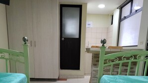 Una habitación con dos camas verdes, un armario blanco, una puerta negra, un lavamanos y una ventana.