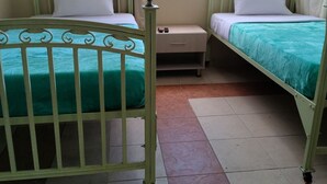Una habitación con dos camas individuales, una mesita de noche pequeña, una ventana con cortinas y vistas a edificios.