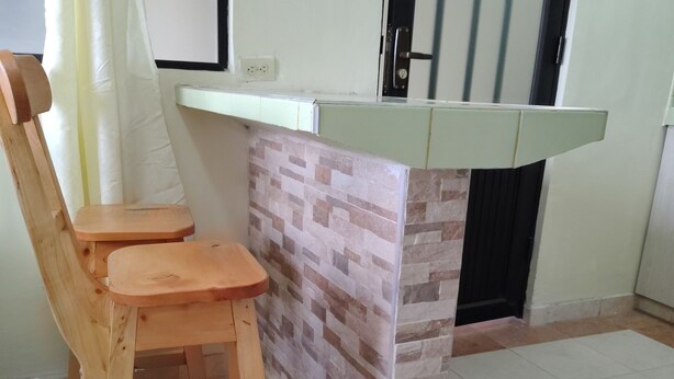 Una pequeña cocina con una silla y un banco de madera, un salpicadero de azulejos y una encimera blanca.