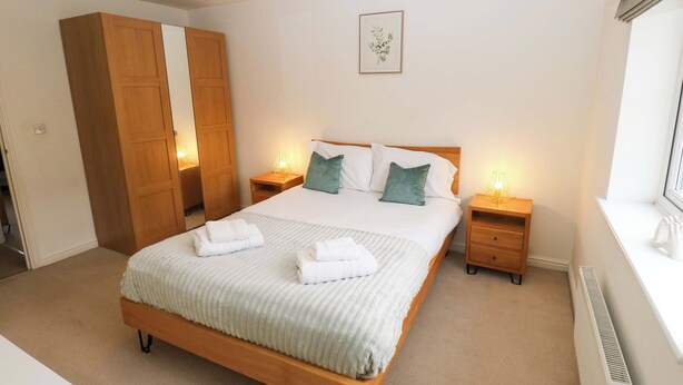 Une chambre bien rangée, avec un grand lit, une armoire en bois, des tables de chevet avec des lampes et un radiateur.